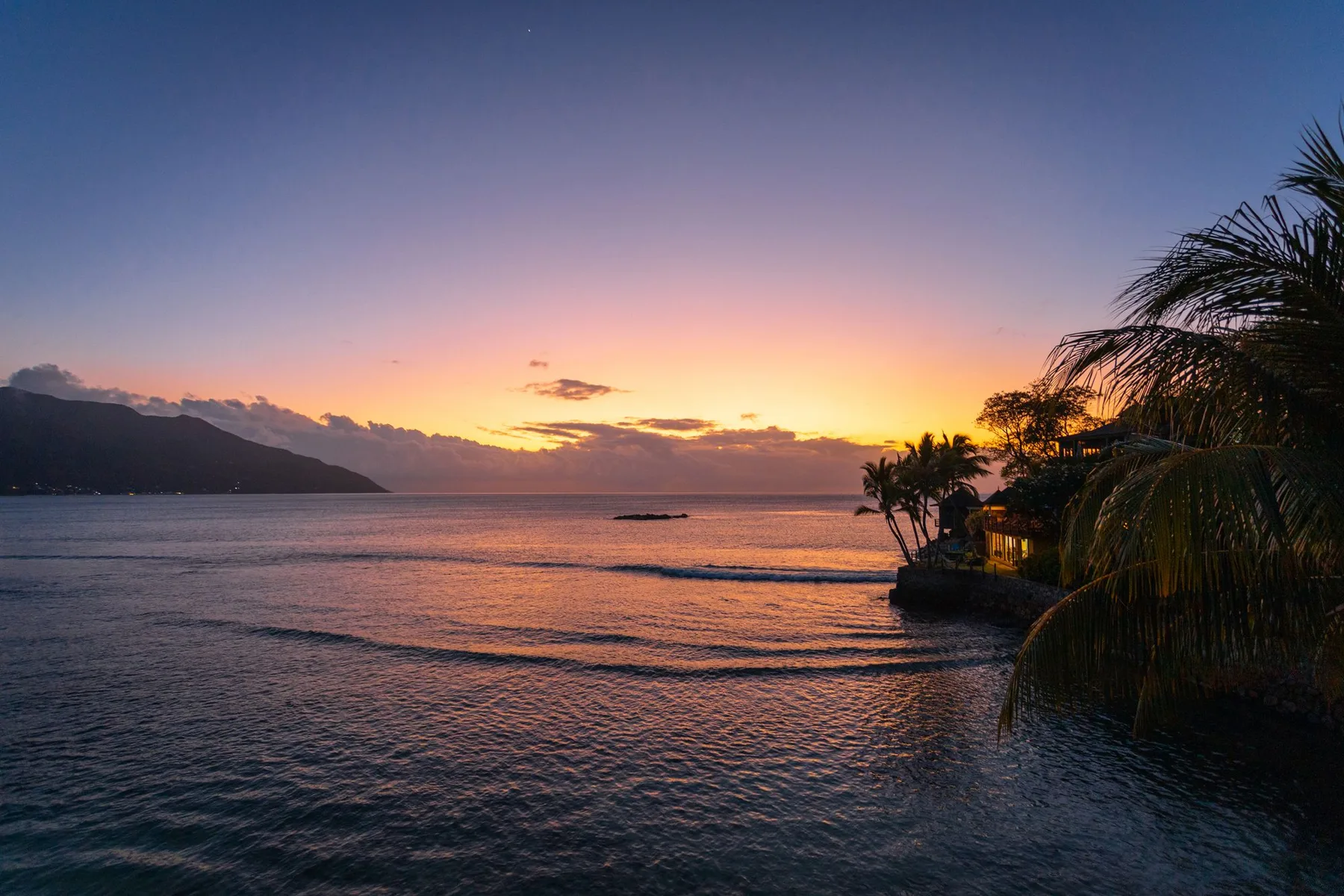 Sunset over calm water beside a forested headland
